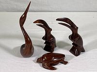 Group photo of four carved hardwood figures including three birds and one turtle, arranged on a white surface
