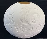 Front view of the round white porcelain vase showing the detailed low relief Northwest Coast art design.