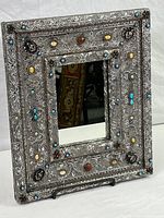 Full view of embossed metal framed mirror with decorative colored stones.