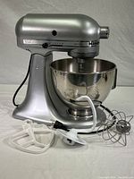 Full view of silver/pewter KitchenAid Artisan stand mixer with bowl attached and accessories laid out in front