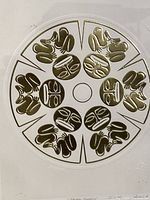 Close-up of circular gold foil embossed artwork showing stylized tribal animal and face motifs.