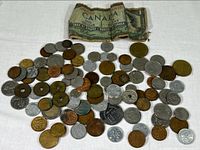 Photo shows a mixed collection of coins and a Canadian one dollar banknote from 1954 on white background, coins in copper, silver, and bronze shades scattered around.