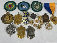 Full assortment of medals, pendants, pins, and scouting badges including cloth patches and ribboned medal on neutral background.