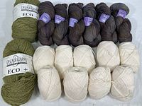 Photo showing 2 skeins olive green Cascade Yarns Eco+ and 6 skeins muted brown/gray Dream Classy yarn plus 9 off-white skeins