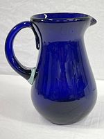 Front and side view of a large cobalt blue glass pitcher with spout and handle, showing size and shape.