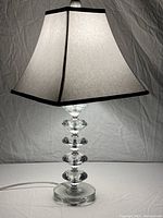 Modern table lamp illuminated to show detailed cut glass stacked base and lined fabric shade with black trim.
