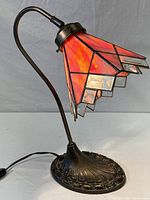 Full view of the stained glass table lamp showing the curved metal arm, colorful geometric glass shade, and round textured base.