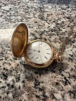 Open hunter case showing white enamel dial with Roman numerals, subsidiary seconds and winding crown.