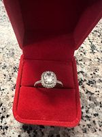 Front view of ring in red velvet box showing cushion cut center and halo