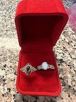 Two sterling silver rings with different stones in a red velvet ring box on a granite surface, showing detailed views of the ring faces and settings.
