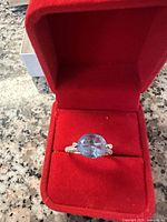 Close-up photo of 925 silver ring with large oval blue stone inside red velvet box on a granite surface.