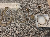 Full view of jewelry lot spread on granite surface showing necklaces, rings, bracelets, earrings, and charms.