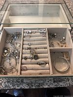 Top-down view showing assorted rings, earrings, bracelets, and necklaces organized in custom jewelry box compartments and ring slots.