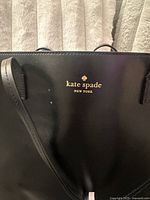Close-up of the front embossed gold Kate Spade New York logo on black leather purse.