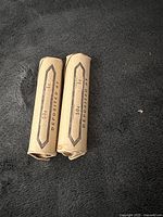 Two rolled paper coin wrappers for 50 cents each, lying on a textured dark surface