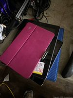 Photo of four iPads with two different cases visible on some devices, stacked together on a surface with some cables and objects in background.