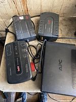 Four APC battery backup/surge protector units placed on a surface, showing their top and side views with power cords and outlets visible.