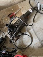 Bosch angle grinder with taped power cord on tiled floor, power cord looped around the tool, side handle attached, cutting disc in place.