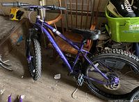 Full view of purple Huffy mountain bike frame with off-road tires, partially assembled, with visible handlebar, seat, and wheels.