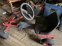 Kids red four-wheeled pedal go-kart showing steering wheel, seat, and frame details.