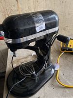 Black KitchenAid Professional 6500 stand mixer with attached wire whisk on a flat surface, plugged into power.