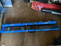 Pair of blue Mastercraft folding sawhorses with black tops, lying on wooden floor among tools and equipment.