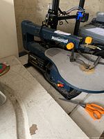 Photo showing Mastercraft scroll saw on a workbench, includes orange scissors nearby.