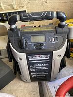 Front view of the MotoMaster Eliminator Booster Pack showing handle, control panel with display, switch, buttons, USB ports, and front label with specifications.