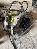 Photo of a Ryobi electric circular saw with blade and power cord, placed on a tiled surface.