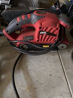 Red and black Skil belt sander with cord, placed on floor surface. Handle and main unit visible.