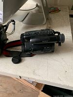 Photo showing black Sony Handycam video camera with 8x zoom and red/black hand strap placed on a wooden surface.
