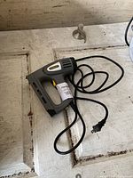Photo of Stanley electric staple tool placed on a light-colored wooden surface, showing the device and attached power cable with plug.