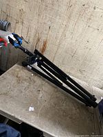 Black Tripped bicycle repair stand folded and resting on a table, shows clamp and tripod legs.