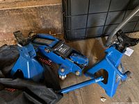 Blue hydraulic trolley jack and two blue steel axle stands on floor with black fabric underneath