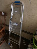 Photo of the two step folding aluminum ladder showing the front side, blue safety grips on top handle, two wide steps, and rubber feet on bottom for slip resistance.