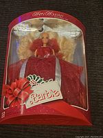 Front view of Barbie doll in original box, showing red dress and holiday bow.