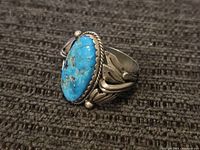 Angled front view showing large oval turquoise cabochon set in twisted-wire bezel on sterling silver band