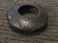 Side view of the round black pottery bowl showing metallic silver grid pattern and part of the top opening.