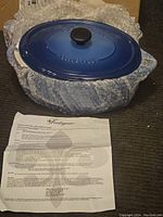 Fontignac cast iron Dutch oven with blue enameled lid, wrapped in bubble wrap, showing embossed brand name on lid and original instruction sheet below.