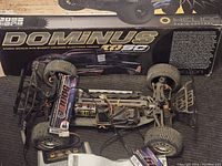 Dominus 10SC RC truck chassis without the body, showing tires, suspension, wiring, and battery pack inside original box.