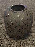 Full view of the rounded black pottery vase with geometric pattern designs on its surface showing polished finish and narrow opening.