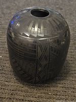 Side view of a small black pottery vase showing geometric pattern designs etched into the surface in a shiny black finish.