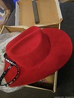 Red Bailey hat placed inside an open box with plastic wrapping, showing hat profile and strap.