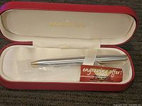 Sheaffer pen in red case with cream lining and gold Sheaffer logo, pen still in plastic wrap, engraving offer card visible.
