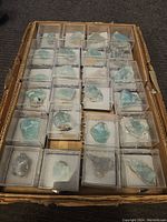 Top view showing rows of blue-green rock specimens in clear individual display cases arranged in a cardboard box.