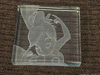 Clear rectangular glass block featuring 3D etched image of Tinkerbell, shown from front view on carpet background.