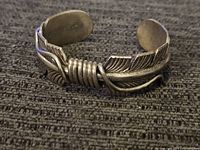 Front view of open cuff highlighting feather design and wrapped wire center.