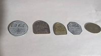 Photo of five Coca Cola tokens from 1904-1915 placed in a line showing varying shapes, sizes, and metal tones.