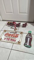 Overview photo of all items in lot including metal Coca-Cola sign, Coca-Cola bottle thermometer, mirror, and cast iron horse and buggy figurines.
