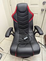 Front view of black and red X Rocker gaming chair with power cord on seat showing splice wrapped in electrical tape.